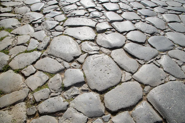 A fragment of the original cobblestone pavement of time-worn stones built by Ancient Rome. Background. Pattern. Gray.