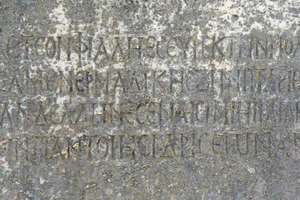 Yarısı silinmiş antik Yunan harfleri eski gri mermer bir levhaya işlenmiş çatlaklar ve kalıplarla kaplı..