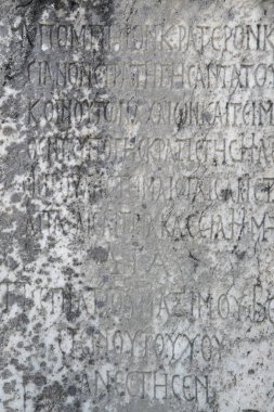 Yarısı silinmiş antik Yunan harfleri eski gri mermer bir levhaya işlenmiş çatlaklar ve kalıplarla kaplı..