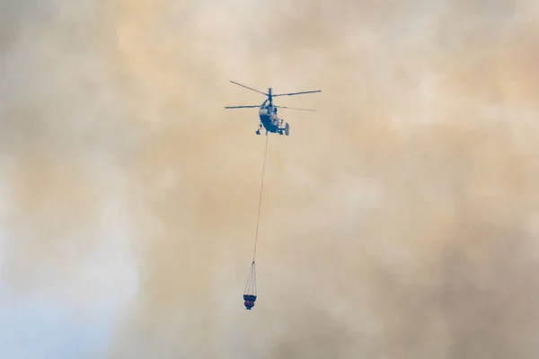 Moskova, Rusya - Ağustos 2019: İtfaiyeciler iş başında. Su dolu süspansiyon gondollu itfaiye helikopteri yangından çıkan siyah-turuncu dumandan çıkan büyük bir yangını söndürüyor..