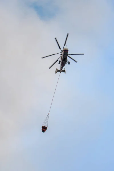 Moskova, Rusya - Ağustos 2019: İtfaiyeciler iş başında. Su dolu süspansiyon gondollu itfaiye helikopteri yangından çıkan siyah-turuncu dumandan çıkan büyük bir yangını söndürüyor..