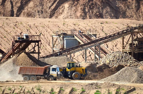 View on the mining quarry for the production of crushed stone, sand and gravel. Crusher plant with belt conveyor, crushing process, grinding stone. Dump trucks transporting sand in the open-pit.