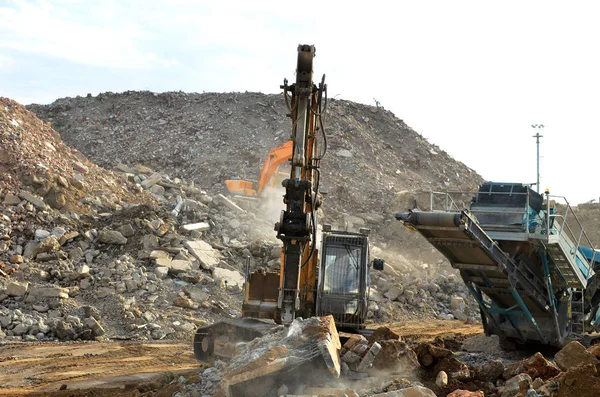 Salvaging and recycling building and construction materials. Excavator with hydraulic hammer work at landfill with concrete demolition waste. Reinforced concrete mobile shredder. Reuse concrete