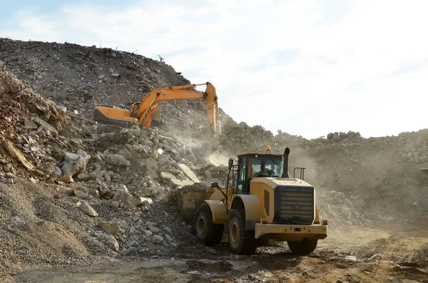 Salvaging and recycling building and construction materials. Industrial waste treatment plant. Excavator and a front-end loader work at landfill with concrete demolition waste. Re-use concrete