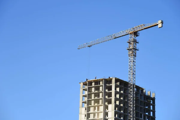 Tower cranes working at construction site against blue sky. Crane lifting a concrete bucket. Construction process of the new residential buildings. Transportation blocks and pouring of the cement mix