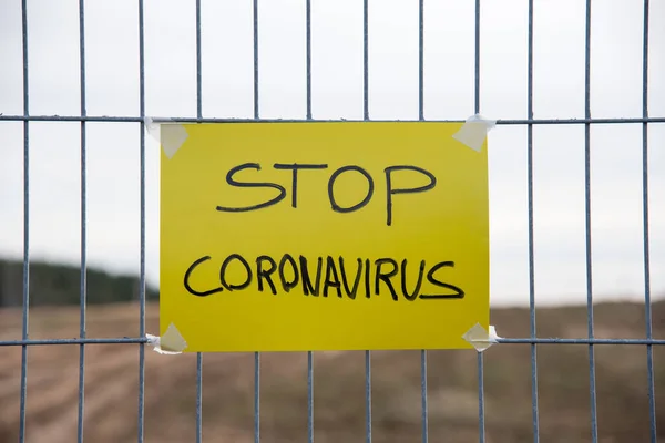 STOPP CORONAVIRUS Text auf der gelben Platte an einem Maschendrahtzaun. Quarantäne-Gebiet COVID-19. Ausbruch der Coronavirus-Epidemie hat zur Schließung von Grenzen, Schulen, Flügen, Reisen, Straßen, U-Bahnen geführt — Stockbild Stopp Coronavirus Text Auf Der Gelben Platte Einem Maschendrahtzaun Quarantäne — Stockfoto