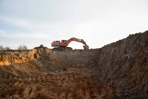 Excavator during earthmoving work at open-pit mining on blue sky background. Loader machine with bucket in sand quarry. Backhoe digging the ground for the foundation and for laying sewer pipes