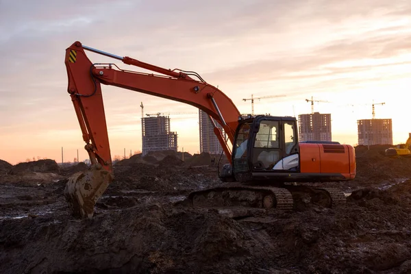 Excavator on earthworks at construction site on sunset background. Backhoe digs ground for the foundation and for paving out sewer line. Construction machinery for excavating