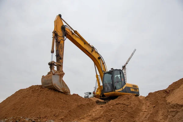 Excavator at earthworks on construction site. Backhoe loader digs a pit for the construction of the foundation. Digging trench for laying sewer pipes drainage in ground. Earth-Moving Heavy Equipment