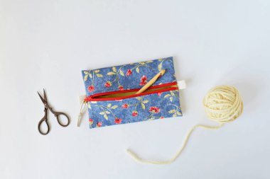 El yapımı fermuar kesesi, örgü kancası, sarı iplik ve makas beyazın üzerinde.
