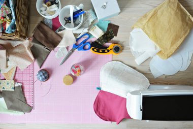Yaratıcı karmaşa: kumaş kırıntıları, iplik, makas, döner kesici, dikiş malzemeleri, paspas, yorgan, iğne, iğne, yorgan cetveli, ahşap masa üzerine dikiş makinesi
