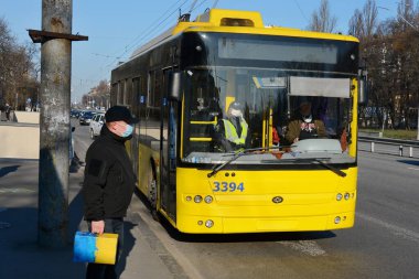 KYIV, UKRAINE - 25 Mart 2020 - COVID-19 Coronavirus salgınıyla bağlantılı olarak karantina sırasında tıbbi maskeli insanlar otobüsü bekliyor
