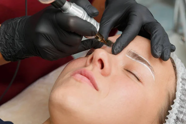 The master applies eyebrow makeup paint to the client with a typewriter. — Stock Photo, Image