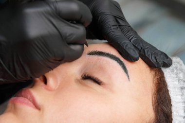 Usta, dövme makinesi kullanarak müşteriye kaş maskesi takıyor..