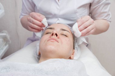 Güzellik uzmanı pamuk pedkullanarak kadının yüzünü yıkar. Temizleme yüzü için hazırlık