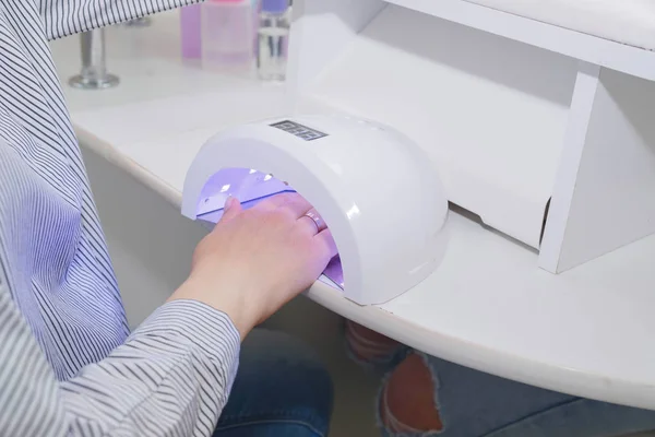 Жінка сушить нігті в ультрафіолетовій лампі в нігтьовому салоні . — стокове фото
