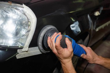 Usta arabanın ön tarafını macun öğütücüsüyle parlatıyor..