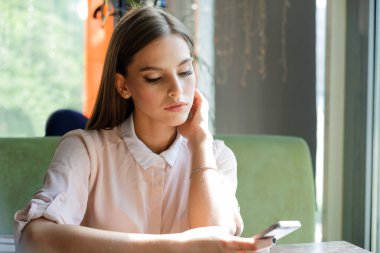 Kız kafede otururken telefonla mesajlar okuyor..