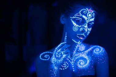 Ultraviyole ışıkta parlayan bir kızın vücudunda ve elinde vücut sanatı.