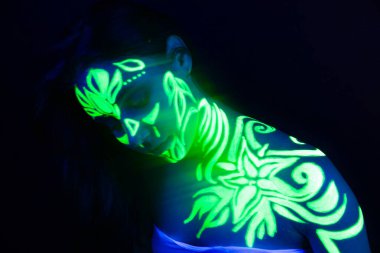 Ultraviyole ışıkta parlayan bir kızın vücudunda ve elinde vücut sanatı.