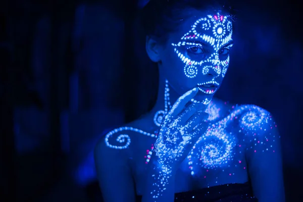 Body art on the body and hand of a girl glowing in the ultraviolet light.
