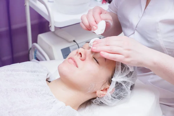 Beautician washes woman's face using cotton pads. Preparing for