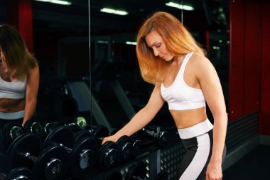 Spor salonundaki halterin yanında bir kız duruyor..