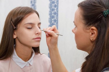 Makyaj yapma süreci. Makyaj sanatçısı modelin yüzünde bir fırça ile çalışıyor. Bir güzellik salonunun iç genç bir kadının portresi. Cilde ton uygulama.