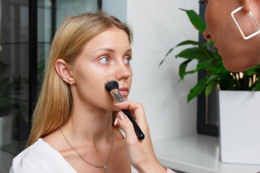 Makyaj yapma süreci. Makyaj sanatçısı modelin yüzünde bir fırça ile çalışıyor. Bir güzellik salonunun iç genç bir kadının portresi. Cilde ton uygulama.