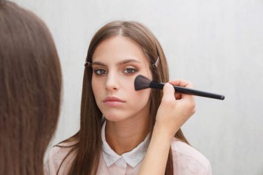 Makyaj yapma süreci. Makyaj sanatçısı modelin yüzünde bir fırça ile çalışıyor. Bir güzellik salonunun iç genç bir kadının portresi. Cilde ton uygulama.