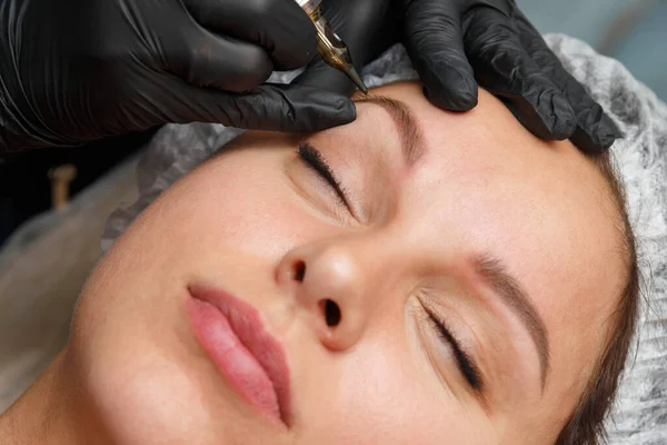 The master applies an eyebrow mask to the client using a tattoo machine. Permanent Eyebrow Makeup Procedure.