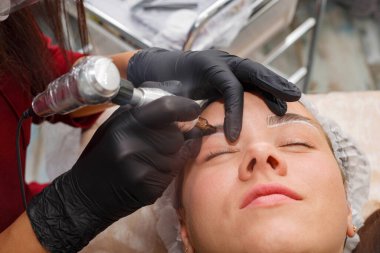 Usta, müşteriye daktiloyla kaş makyajı yapar. Kalıcı Kaş Makyajı Prosedürü.