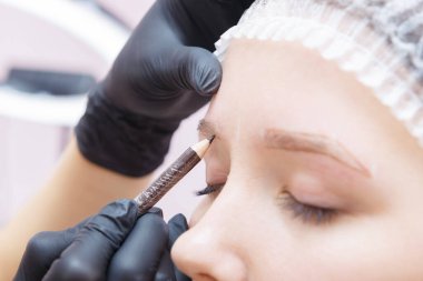 Sihirbaz ameliyattan önce müşterilerin kaşlarını şekillendirir. Kalıcı Kaş Makyajı Prosedürü.
