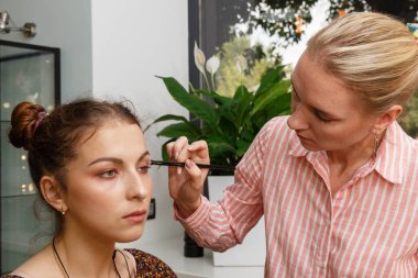 Makyaj yapma süreci. Makyaj sanatçısı modelin yüzünde bir fırça ile çalışıyor. Bir güzellik salonunun iç genç bir kadının portresi. Cilde ton uygulama.