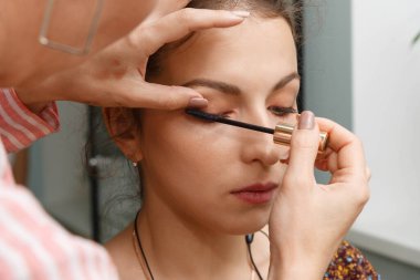 Makyöz, modelin şehvetli kirpiklerini oluşturuyor. Makyaj yapma süreci.