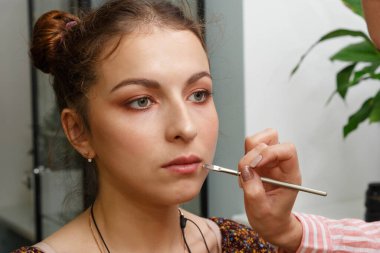Makyaj yapma süreci. Makyaj sanatçısı modelin yüzünde bir fırça ile çalışıyor. Bir güzellik salonunun iç genç bir kadının portresi. Cilde ton uygulama.