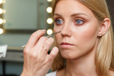 Makyaj yapma süreci. Makyaj sanatçısı modelin yüzünde bir fırça ile çalışıyor. Bir güzellik salonunun iç genç bir kadının portresi. Cilde ton uygulama.