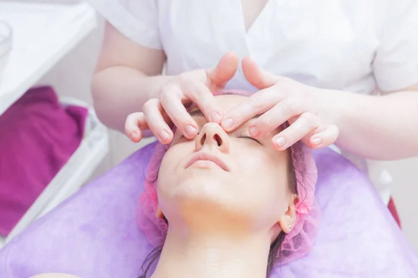 The master conducts the face preparation procedure. Preparation of the client for buccal massage.. cosmetologist makes a buccal massage of the patient\'s facial muscles.