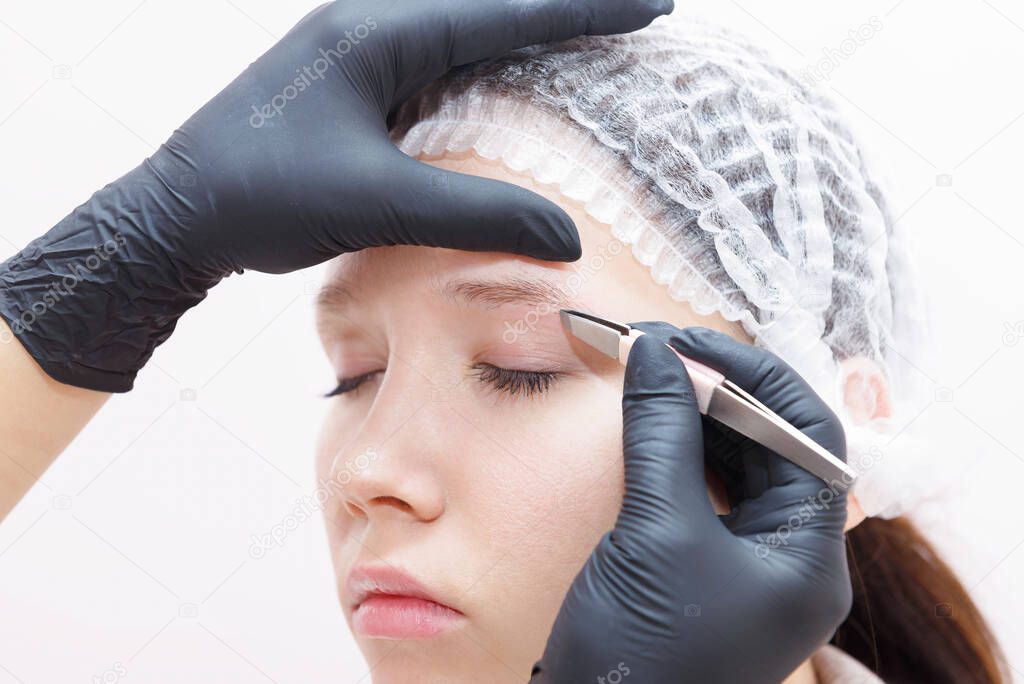 The master removes tweezers with eyebrow hair after the procedure. Permanent Eyebrow Makeup Procedure.