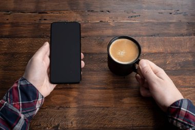 Akıllı cep telefonu kullanan, eve kahve ile masaj yapan bir adam. Siyah ekranlı telefon, mesajlaşma, video görüşmeleri. Evde çalış.. 