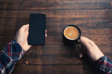 Akıllı cep telefonu kullanan, eve kahve ile masaj yapan bir adam. Siyah ekranlı telefon, mesajlaşma, video görüşmeleri. Evde çalış.. 