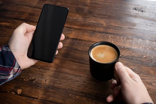 Akıllı cep telefonu kullanan, eve kahve ile masaj yapan bir adam. Siyah ekranlı telefon, mesajlaşma, video görüşmeleri. Evde çalış.. 