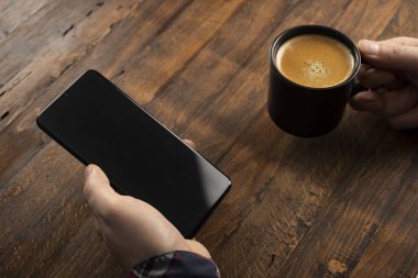 Akıllı cep telefonu kullanan, eve kahve ile masaj yapan bir adam. Siyah ekranlı telefon, mesajlaşma, video görüşmeleri. Evde çalış.. 