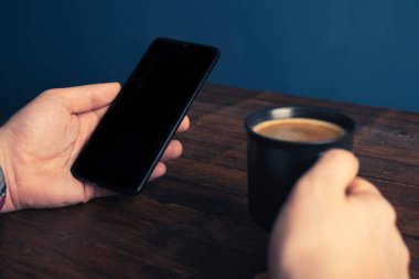 Akıllı cep telefonu kullanan, eve kahve ile masaj yapan bir adam. Siyah ekranlı telefon, mesajlaşma, video görüşmeleri. Evde çalış.. 