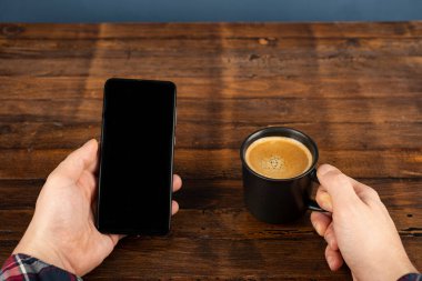 Akıllı cep telefonu kullanan, eve kahve ile masaj yapan bir adam. Siyah ekranlı telefon, mesajlaşma, video görüşmeleri. Evde çalış.. 