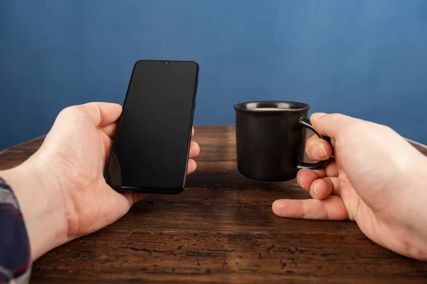 Close up of man using mobile smart phone,sending massages on the home with coffee. Phone with black screen,texting,video calls. Work at home.