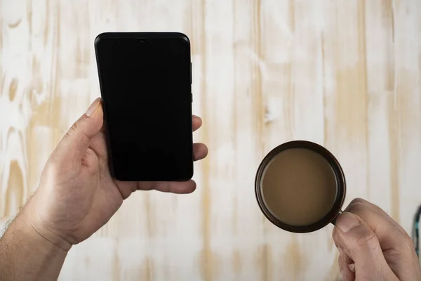 Close up of man using mobile smart phone,sending massages on the home with coffee. Phone with black screen,texting,video calls. Work at home.