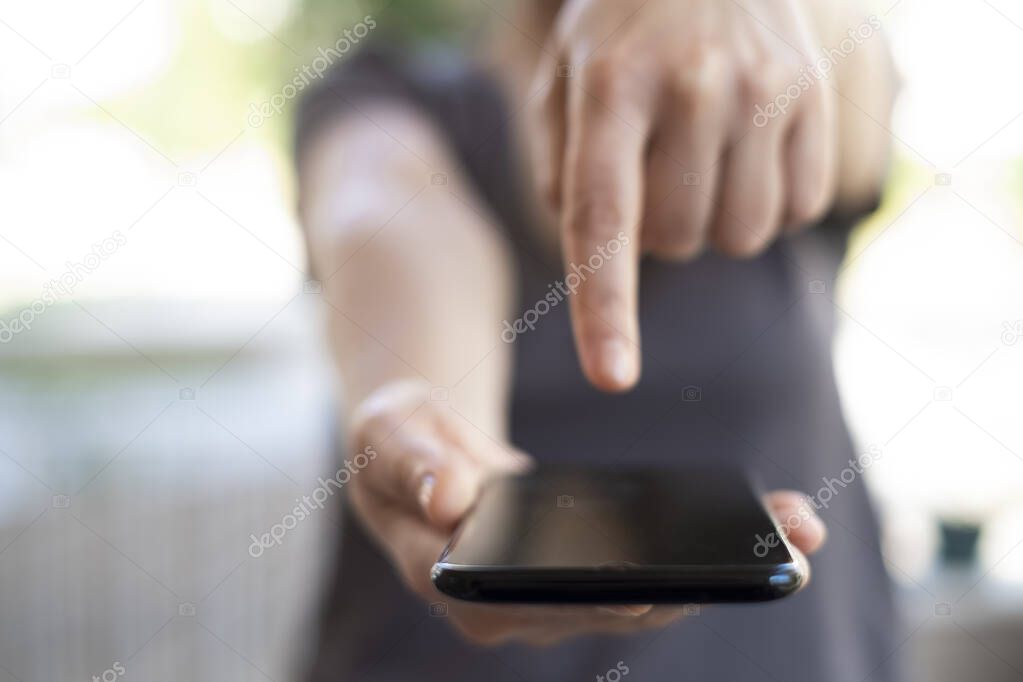 Woman's hands holding black mobile phone with blank screen on thigh and coffee cup in home