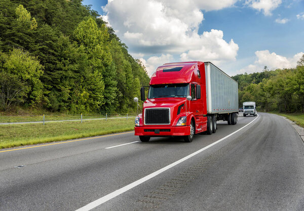 Horizontal shot of a red semi truck going down an interstate highway.