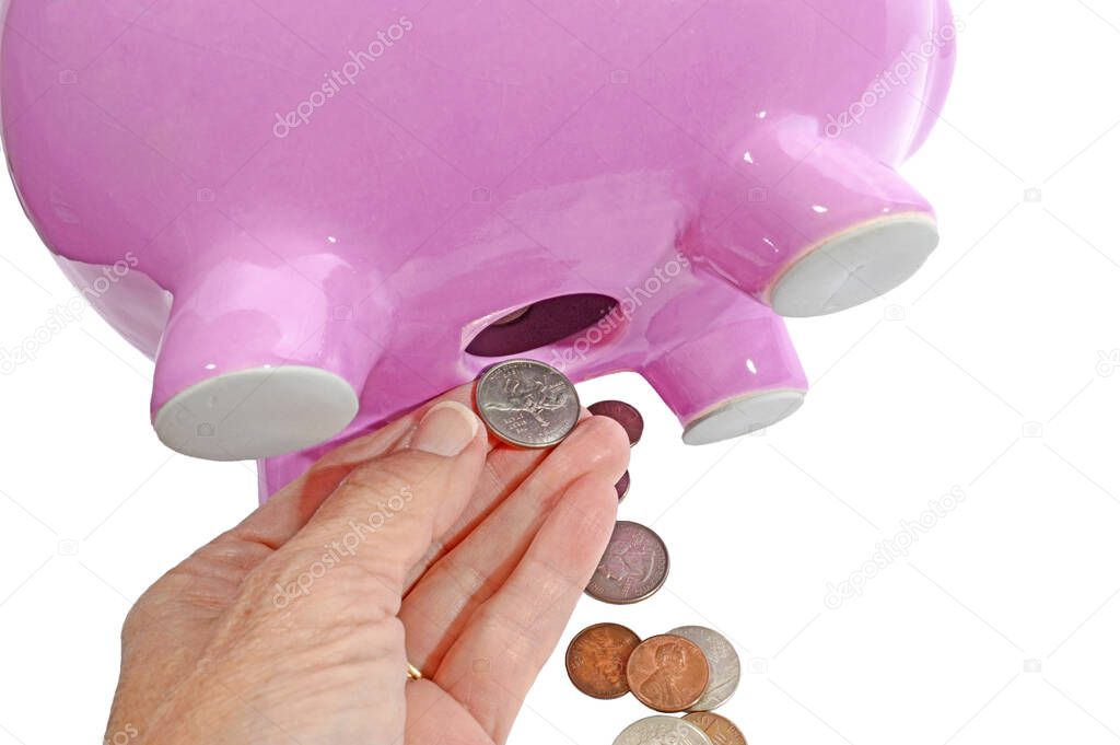 Horizontal close-up shot of a woman's hand pulling coins from the hole on the bottom of a pink piggy bank.  White background.